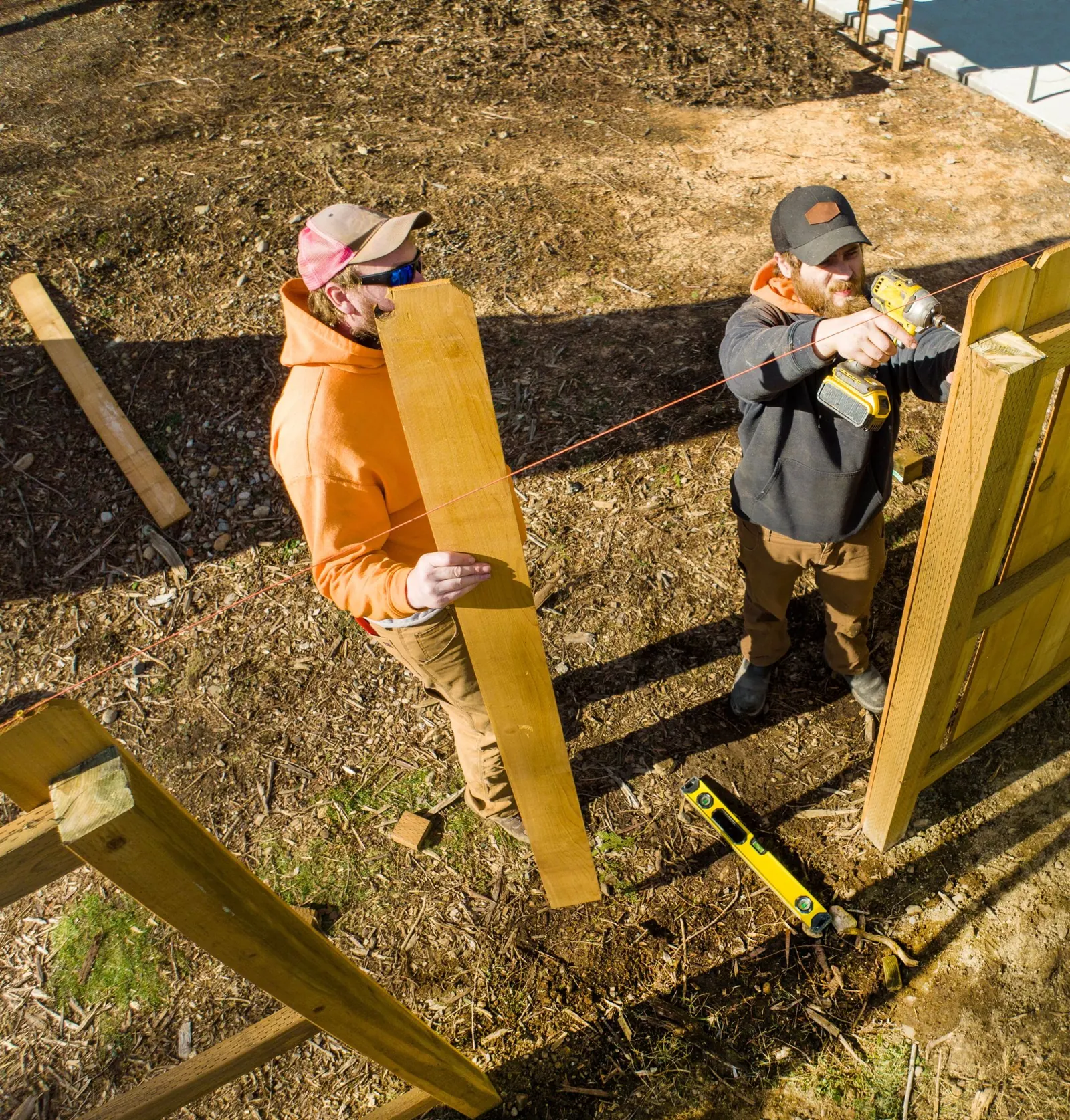 Two installers setting wood fence boards on a sunny day