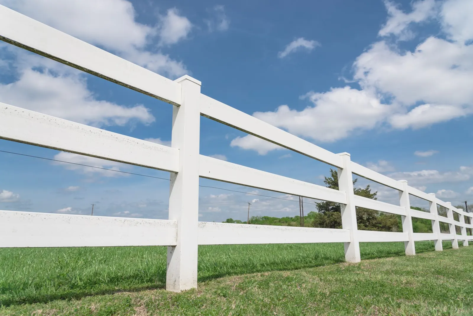 White three-rail vinyl ranch fence under a blue sky