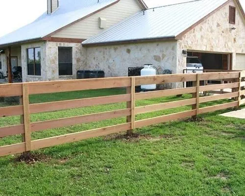 Three-rail wood ranch fence in front of a stone home